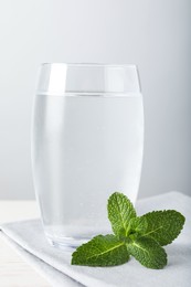 Photo of Glass of soda water, mint and napkin on white wooden table