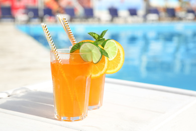 Refreshing cocktail in glasses near outdoor swimming pool on sunny day. Space for text
