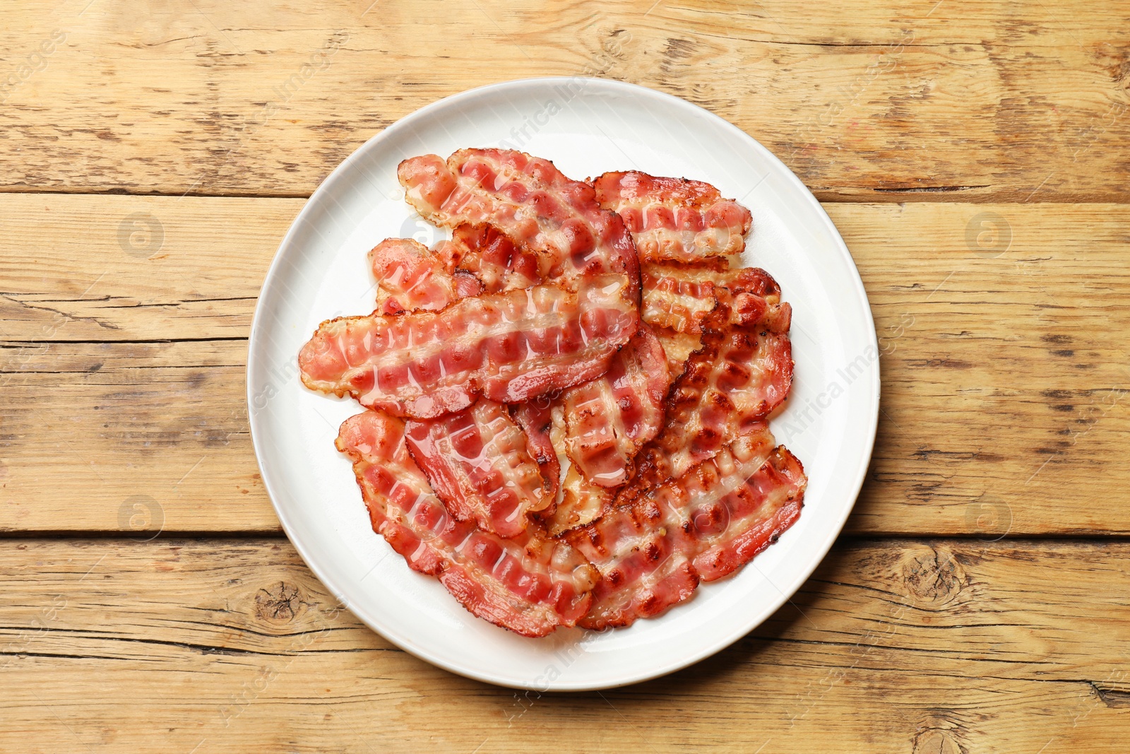 Photo of Plate with fried bacon slices on wooden table, top view