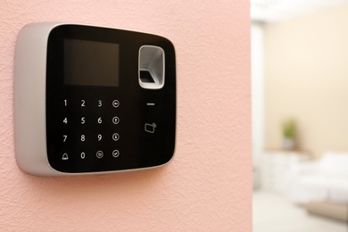 Photo of Modern alarm system with fingerprint scanner on color wall indoors. Space for text