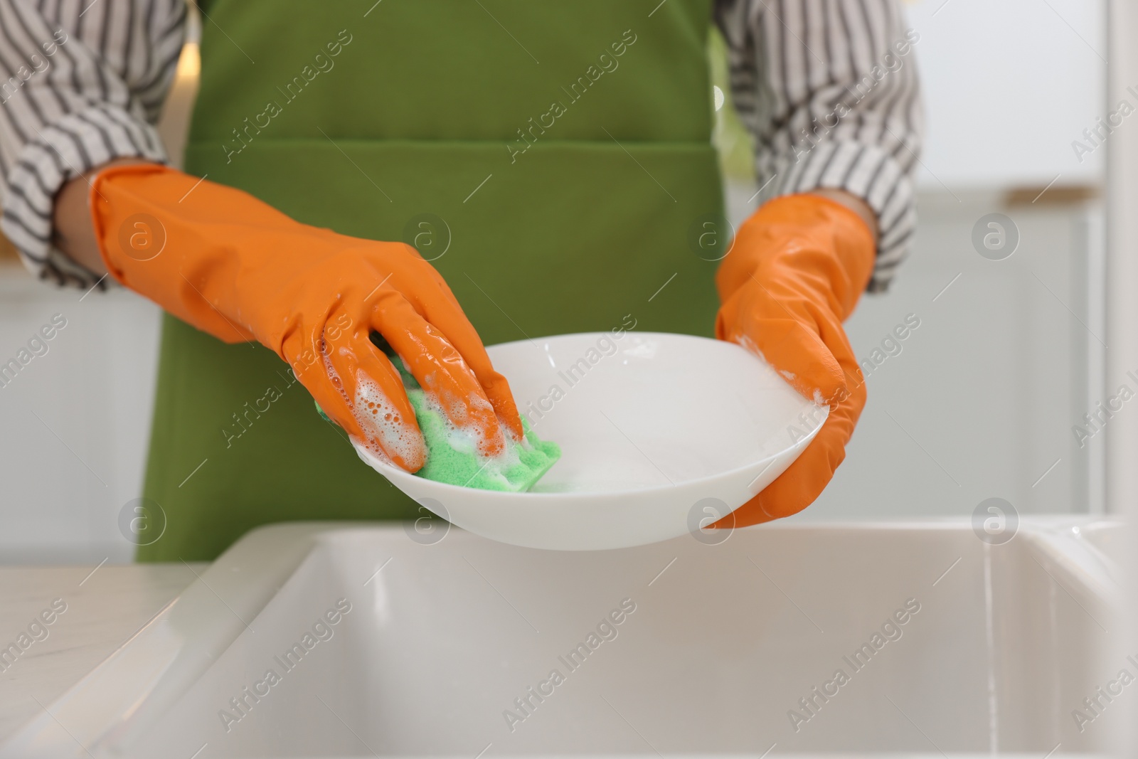 Photo of Woman washing plate above sink in modern kitchen, closeup