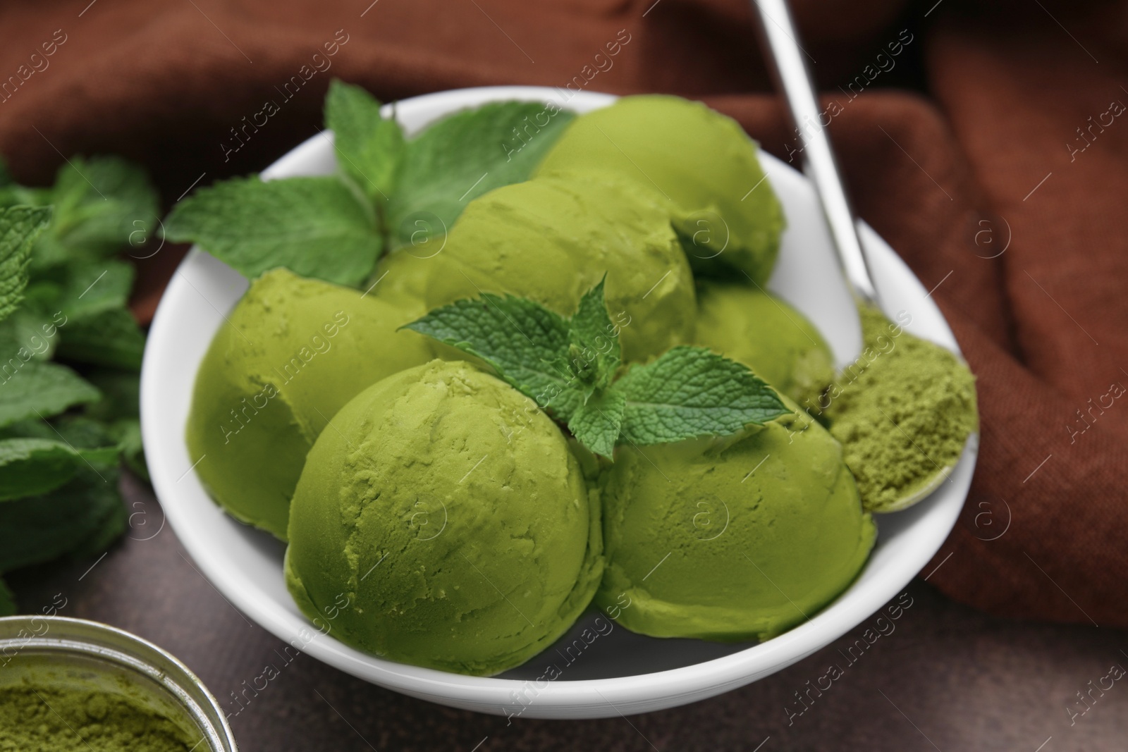 Photo of Tasty matcha ice cream and spoon with powder in bowl on table, closeup