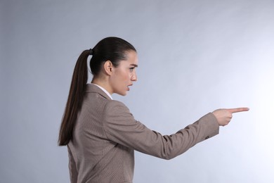 Emotional woman in suit pointing with index finger on light grey background