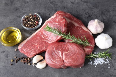 Photo of Raw beef steaks, oil and spices on grey table