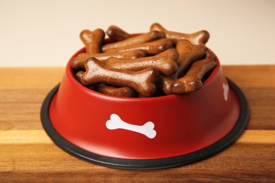 Photo of Red bowl with bone shaped dog cookies on wooden board, closeup
