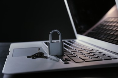Photo of Metal lock, keys and laptop on dark background, closeup. Cyber security concept