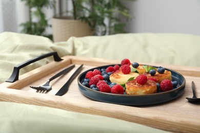 Photo of Tasty breakfast served in bedroom. Cottage cheese pancakes with fresh berries and mint on wooden tray