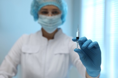 Doctor holding syringe with COVID-19 vaccine on blurred background