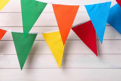 Buntings with colorful triangular flags hanging on white wooden wall. Festive decor