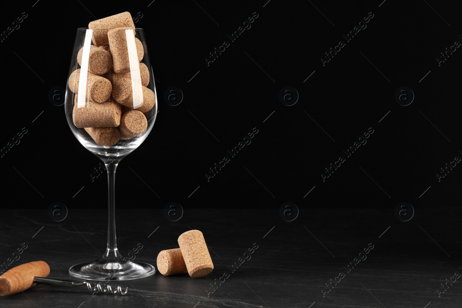 Photo of Glass with wine corks and corkscrew on dark table. Space for text