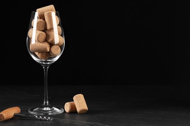 Photo of Glass with wine corks and corkscrew on dark table. Space for text