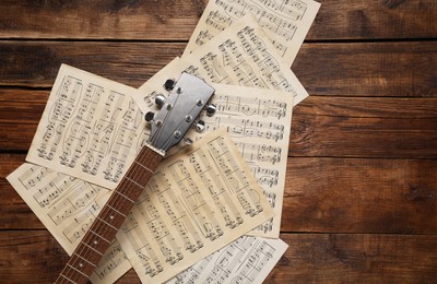 Photo of Paper sheets with music notes and guitar neck on wooden table, top view. Space for text