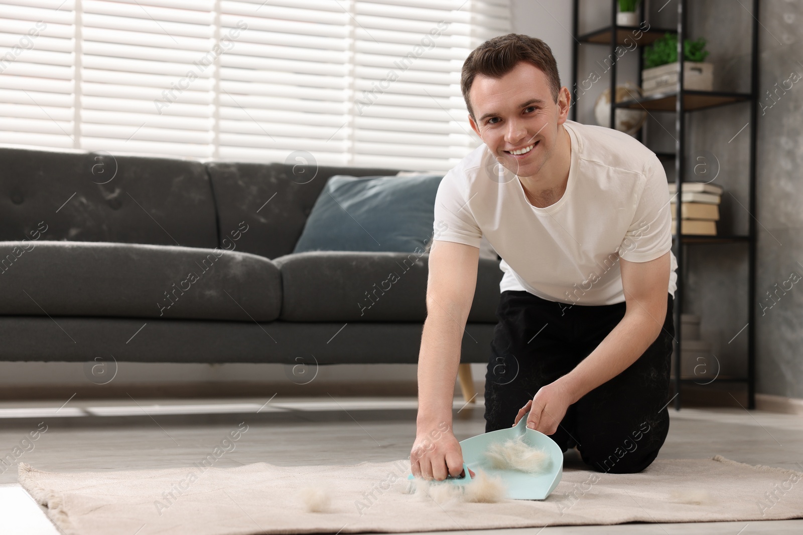 Photo of Smiling man with brush and pan removing pet hair from carpet at home. Space for text