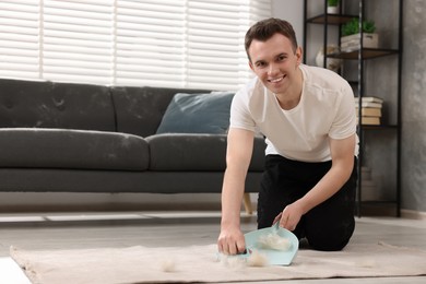 Smiling man with brush and pan removing pet hair from carpet at home. Space for text