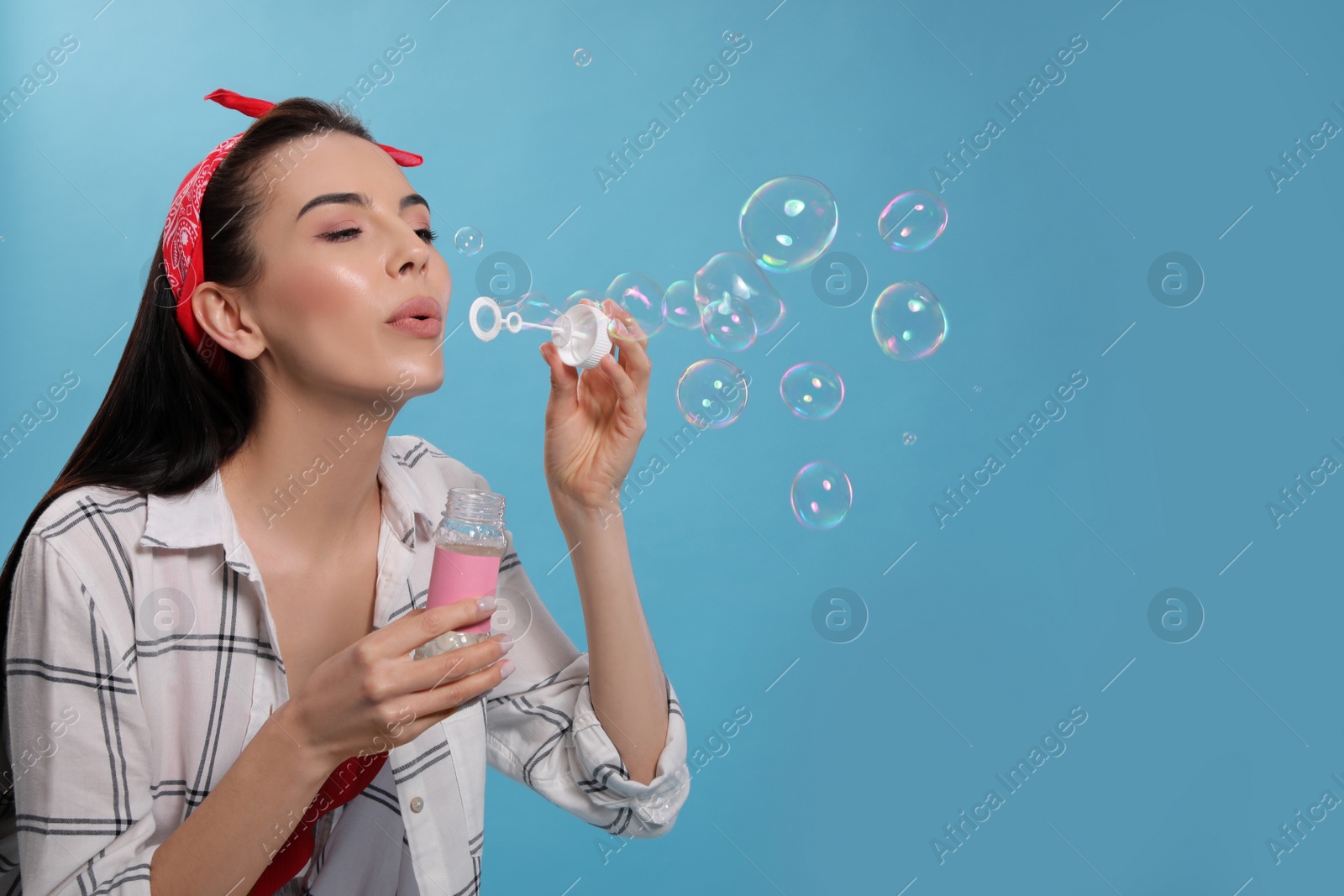 Photo of Young woman blowing soap bubbles on light blue background, space for text