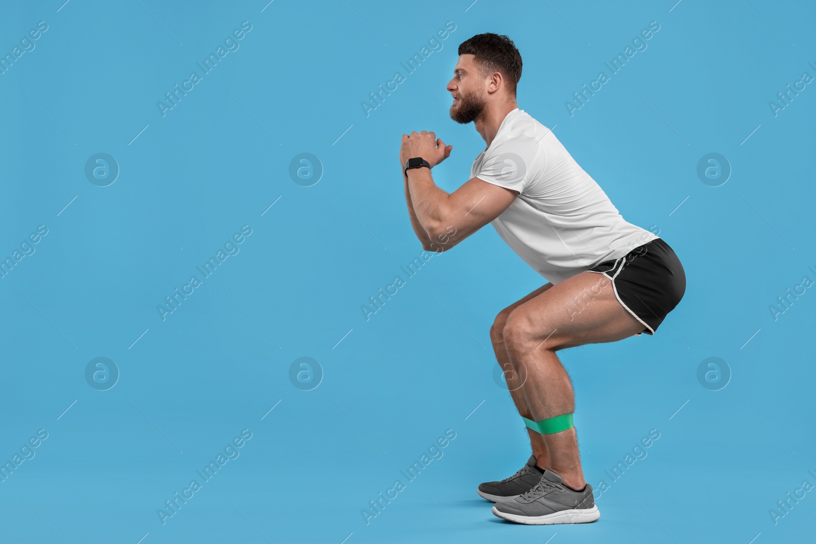 Photo of Young man exercising with elastic resistance band on light blue background. Space for text