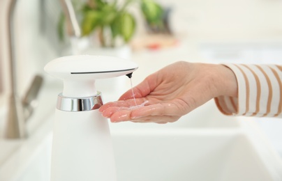 Photo of Woman using automatic soap dispenser in kitchen, closeup