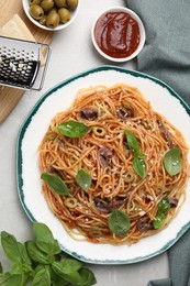 Photo of Delicious pasta with anchovies, tomato sauce and basil on light grey table, flat lay