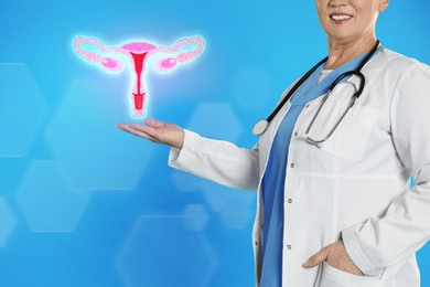 Image of Mature doctor demonstrating virtual icon with illustration of female reproductive system on light blue background, closeup. Gynecological care 
