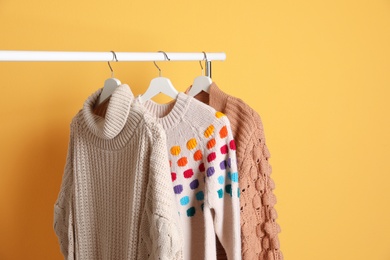 Collection of warm sweaters hanging on rack against color background