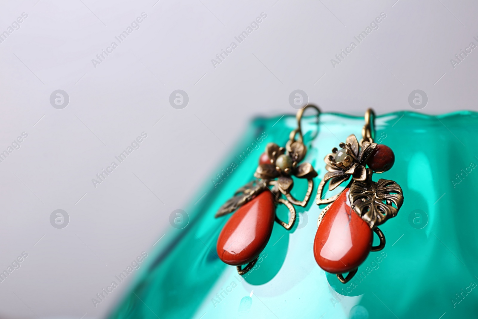 Photo of Beautiful pair of metal earrings with red jasper gemstones on glass stand against light grey background. Space for text