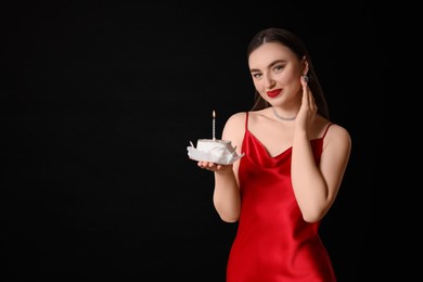 Photo of Attractive young woman holding her Birthday cake with burning candle on black background, space for text