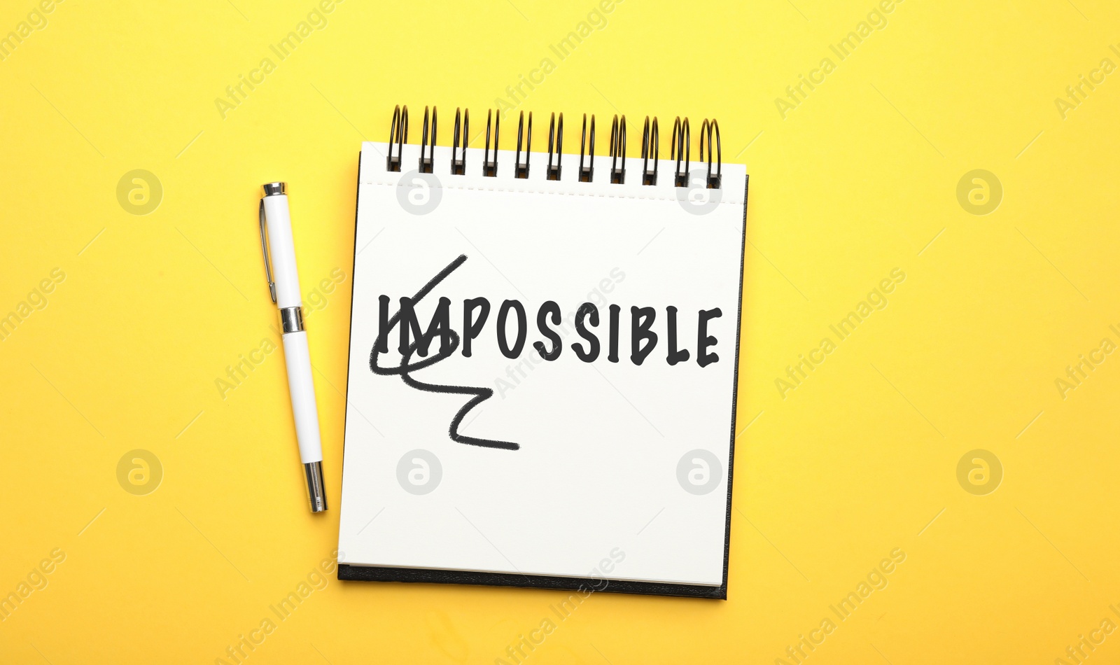 Image of Word IMPOSSIBLE with crossed out letters IM written in notebook and pencil on yellow background, top view. Motivation and positivity