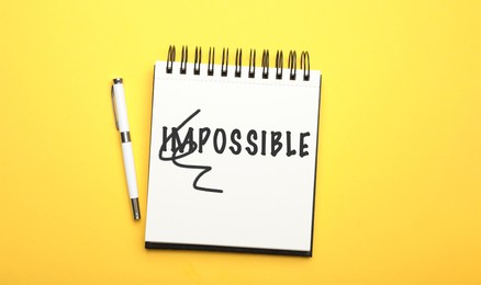 Image of Word IMPOSSIBLE with crossed out letters IM written in notebook and pencil on yellow background, top view. Motivation and positivity