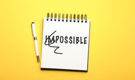 Word IMPOSSIBLE with crossed out letters IM written in notebook and pencil on yellow background, top view. Motivation and positivity