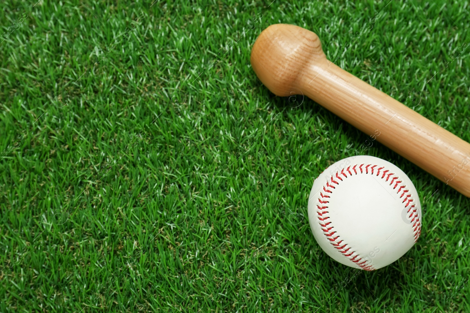 Photo of Wooden baseball bat and ball on green grass, flat lay. Space for text