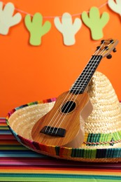 Mexican sombrero hat and ukulele on color table, closeup