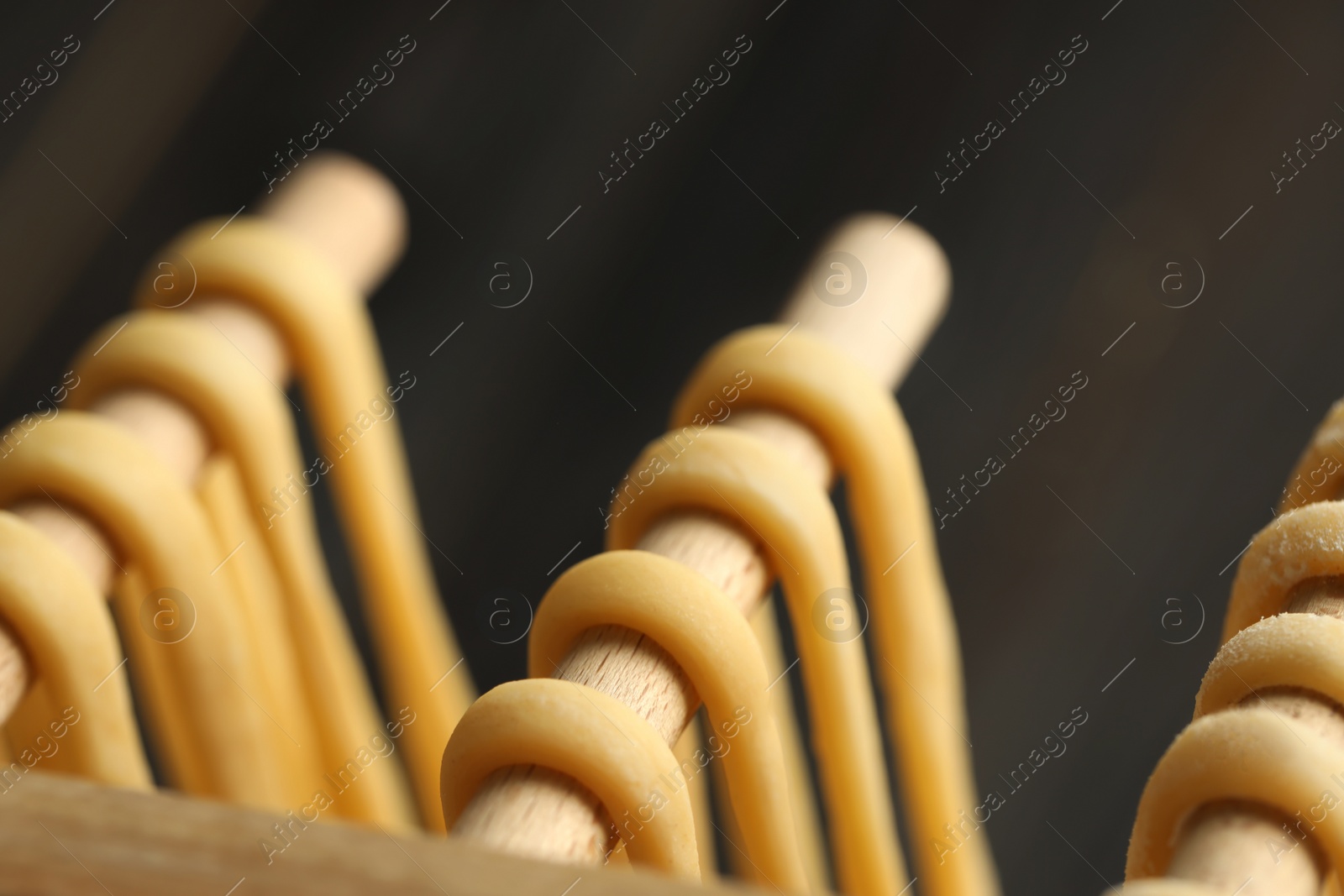 Photo of Homemade pasta drying on wooden rack against dark grey background, closeup