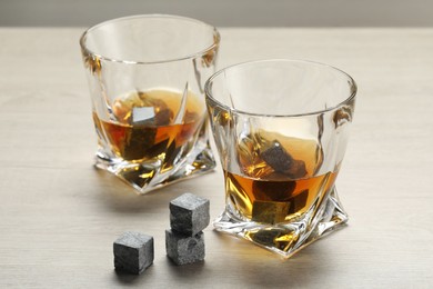 Photo of Whiskey stones and drink in glasses on light wooden table, closeup