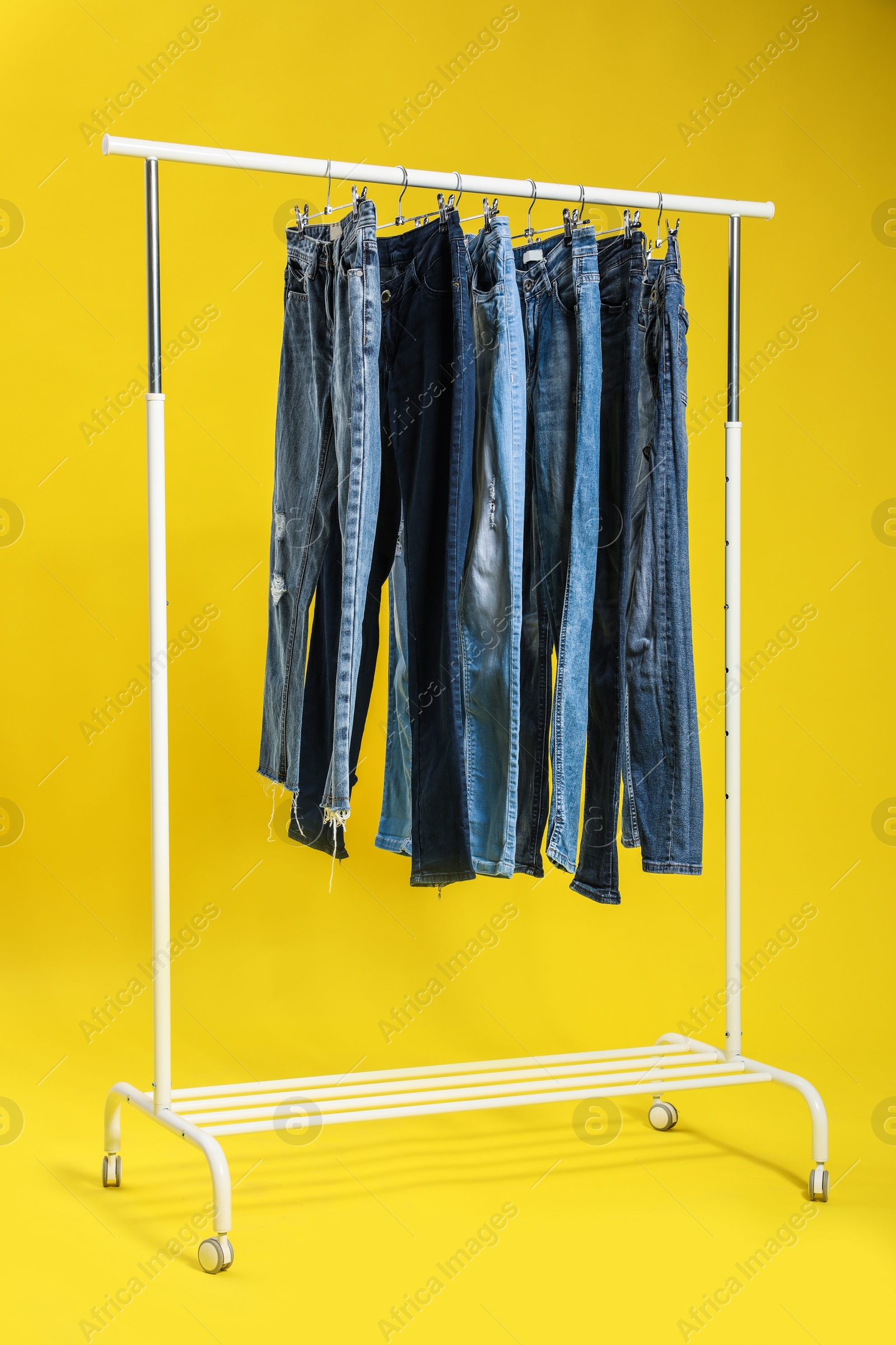 Photo of Rack with different jeans on yellow background