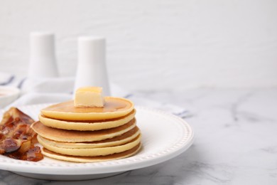 Photo of Delicious pancakes with butter, maple syrup and fried bacon on white marble table. Space for text