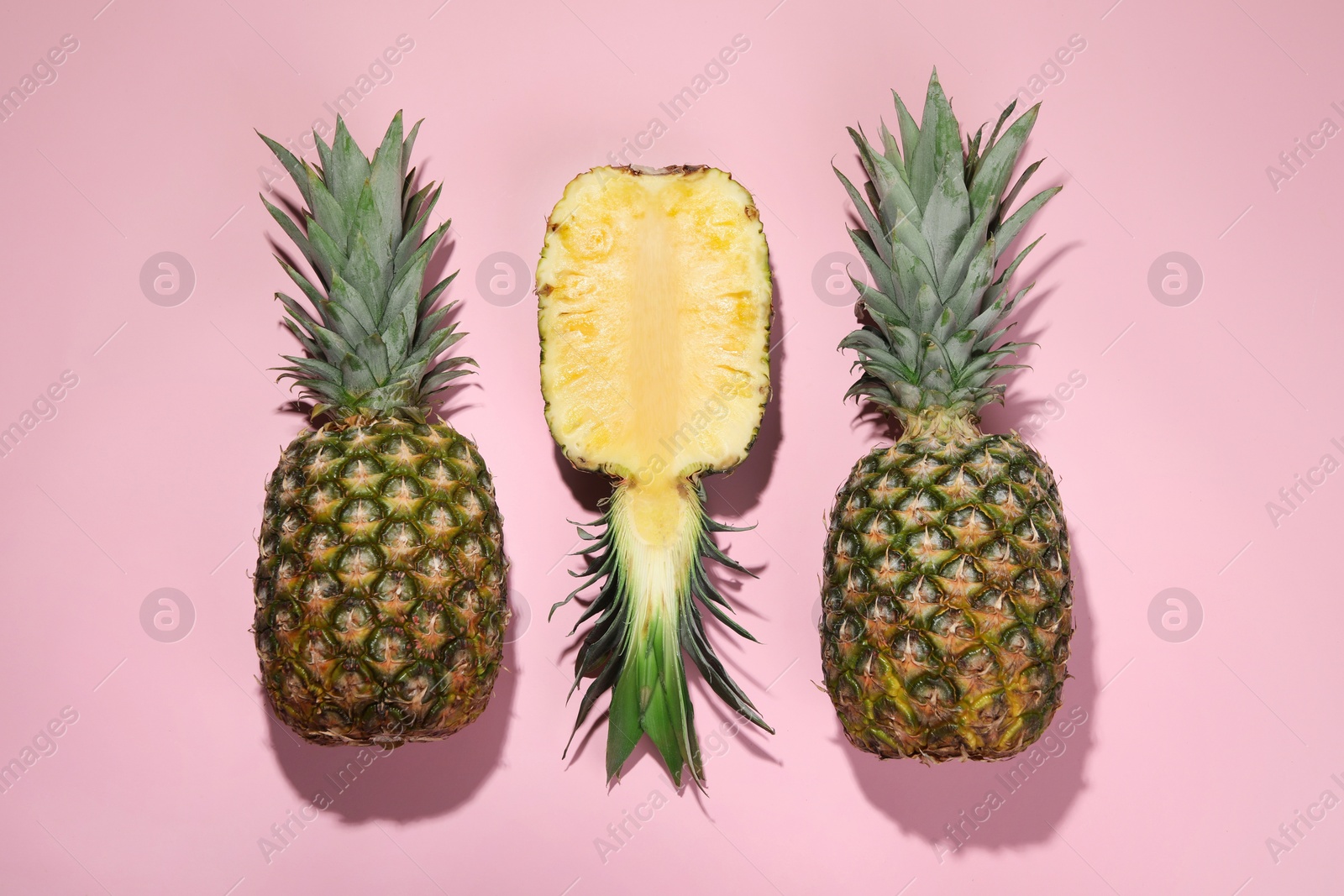 Photo of Whole and cut ripe pineapples on pale pink background, flat lay