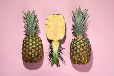 Whole and cut ripe pineapples on pale pink background, flat lay