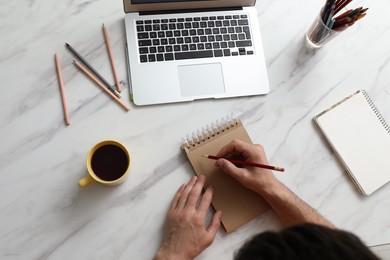 Man drawing in notebook at table, top view. Distance learning