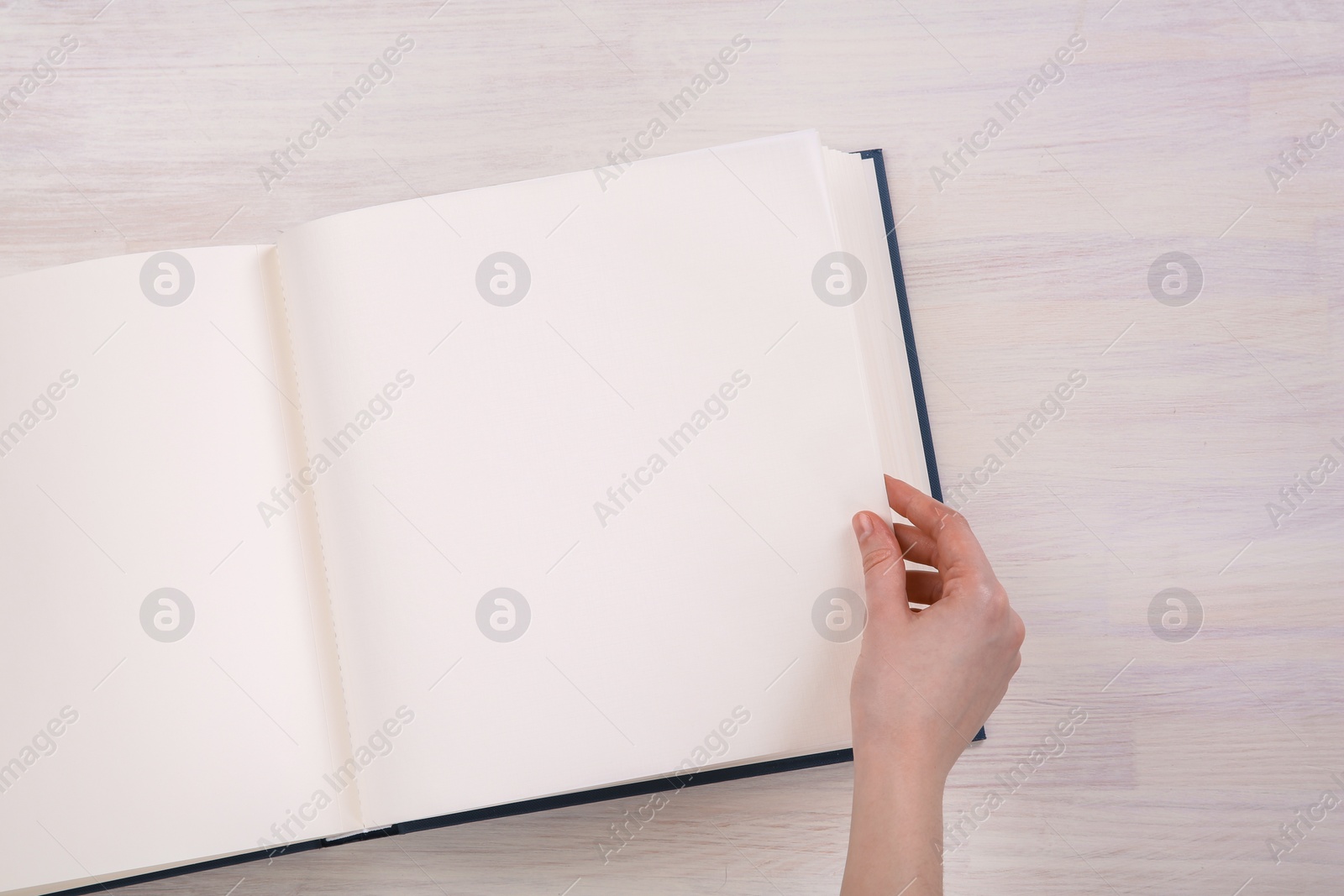 Photo of Woman with open photo album at white wooden table, top view. Space for text