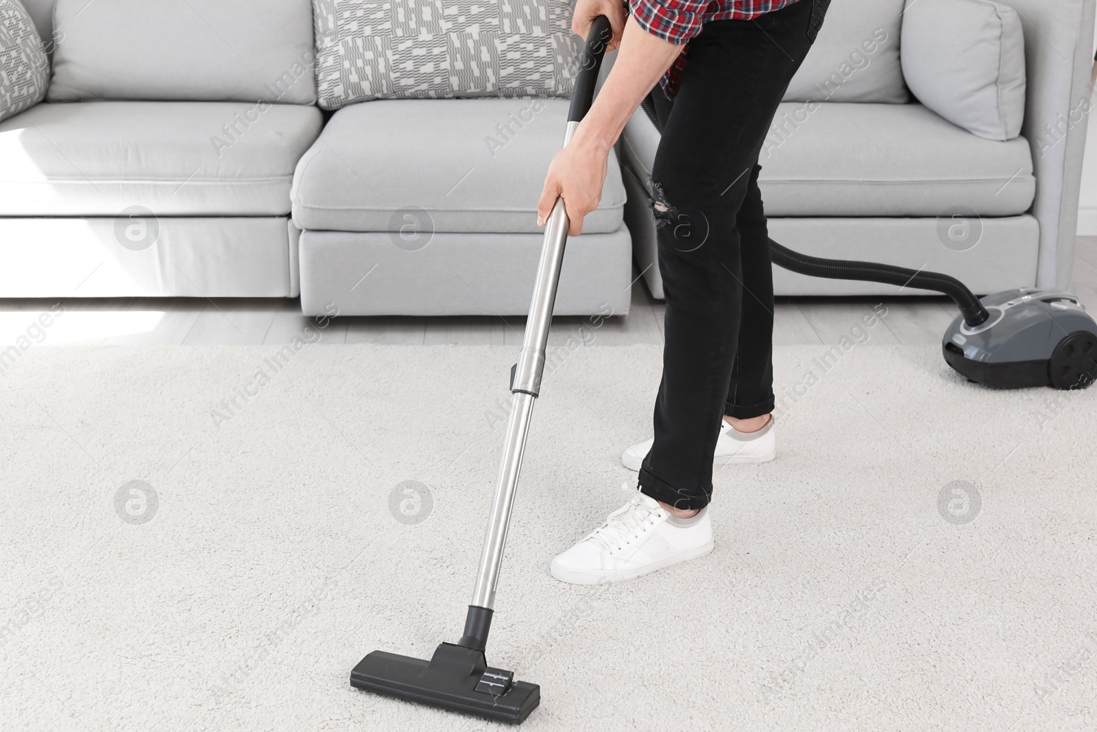 Photo of Young man removing dirt from carpet with vacuum cleaner at home