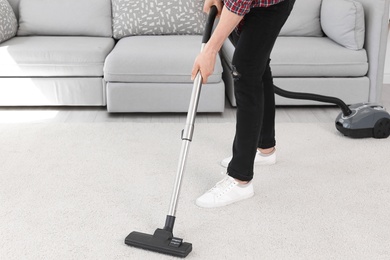 Young man removing dirt from carpet with vacuum cleaner at home