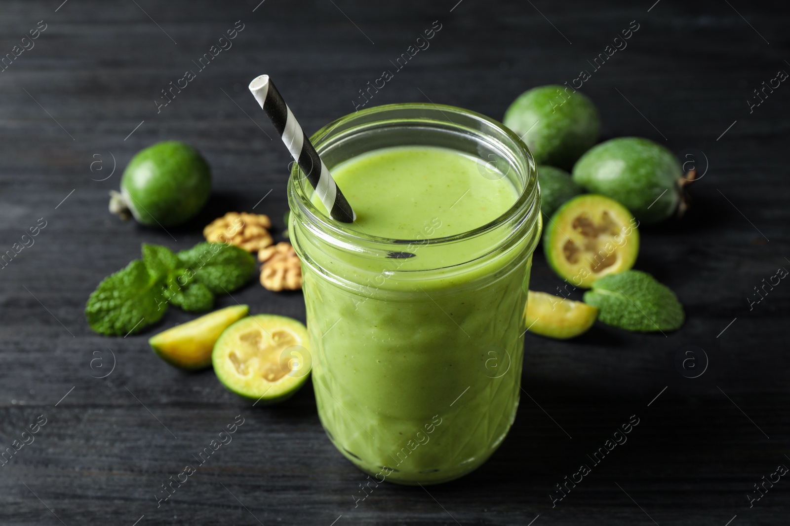Photo of Fresh feijoa smoothie in glass on black wooden table, closeup