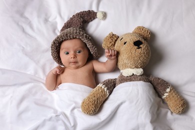 Photo of Cute little baby with toy bear lying under blanket in bed, top view
