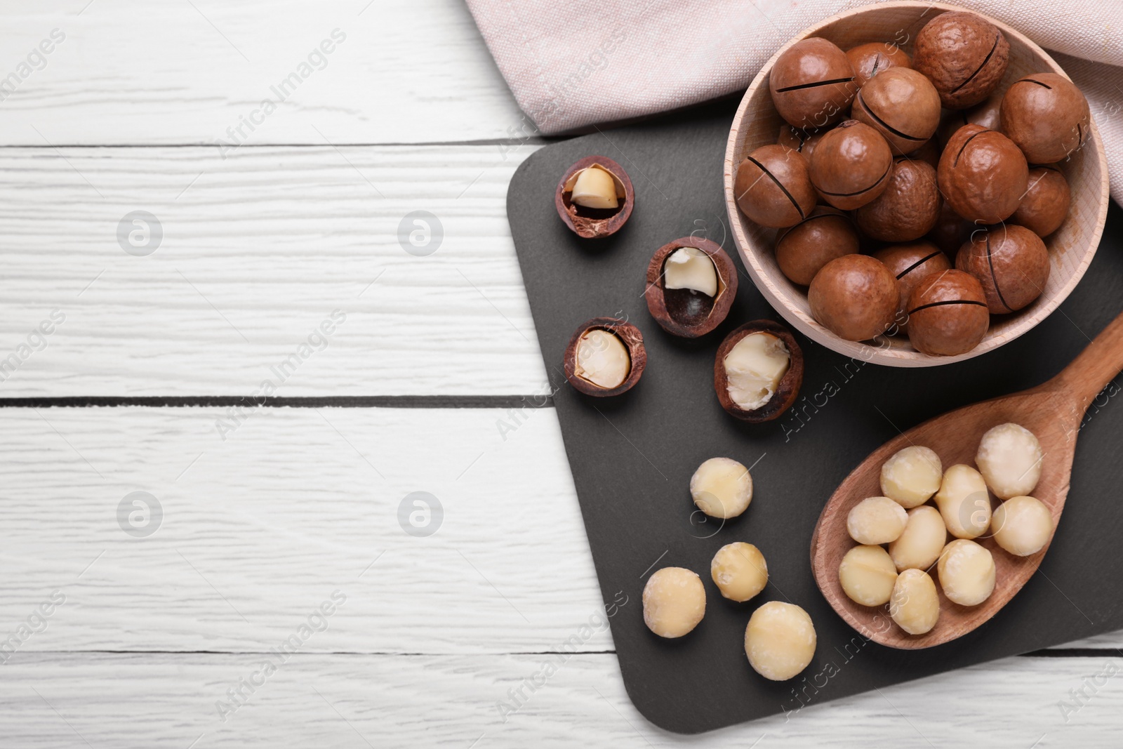 Photo of Delicious organic Macadamia nuts on white wooden table, top view. Space for text