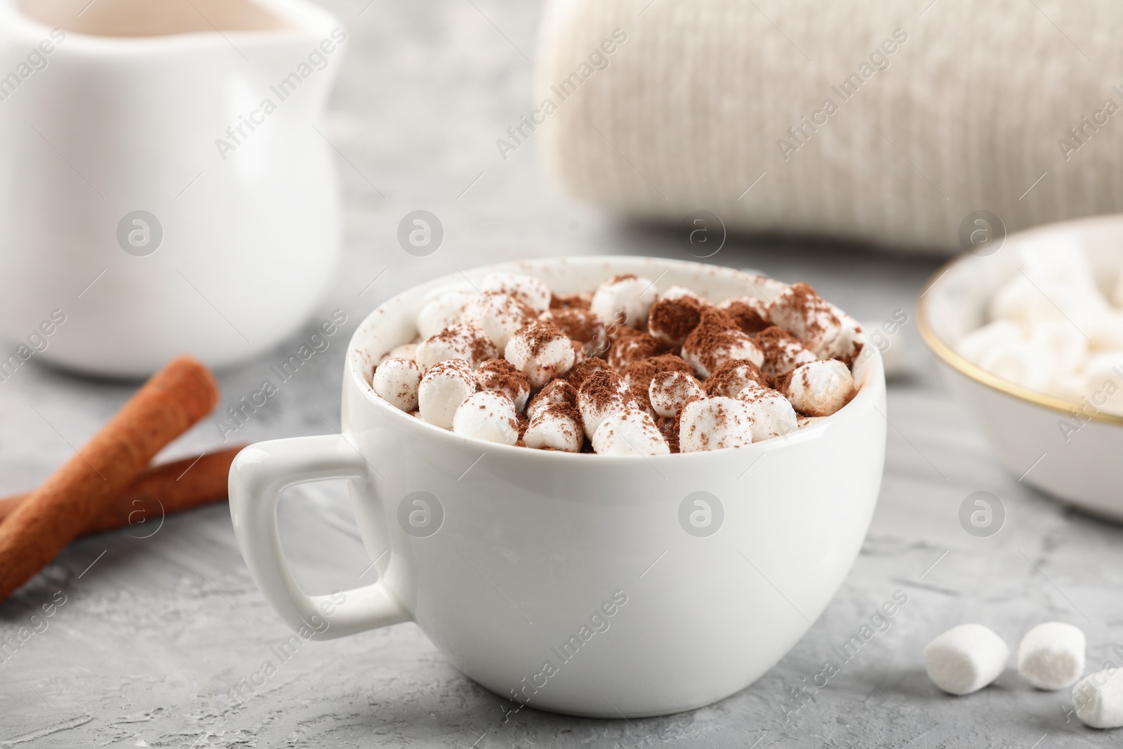 Photo of Cup of aromatic hot chocolate with marshmallows and cocoa powder on gray table, closeup