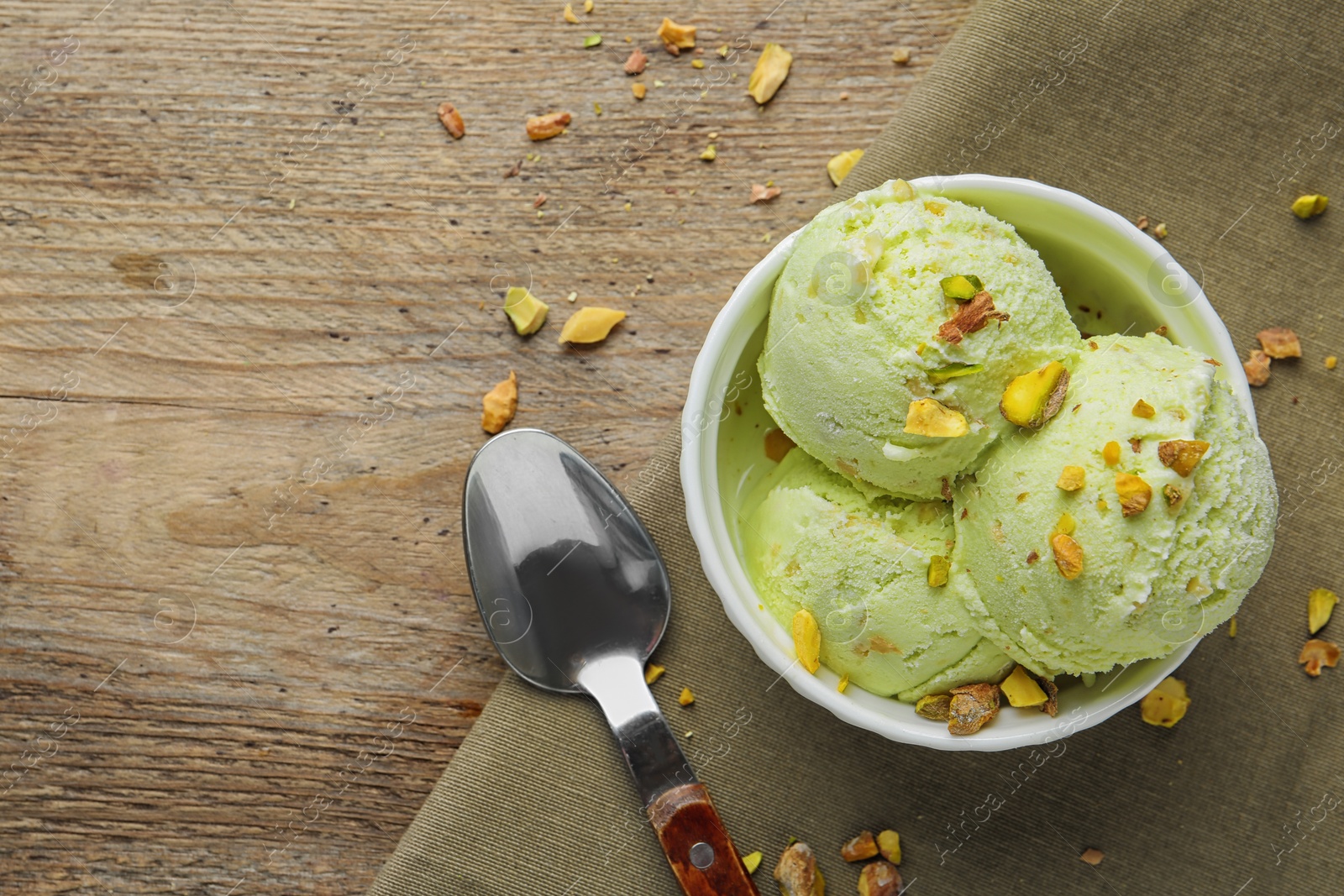 Photo of Delicious green ice cream served in ceramic bowl on wooden table, flat lay. Space for text