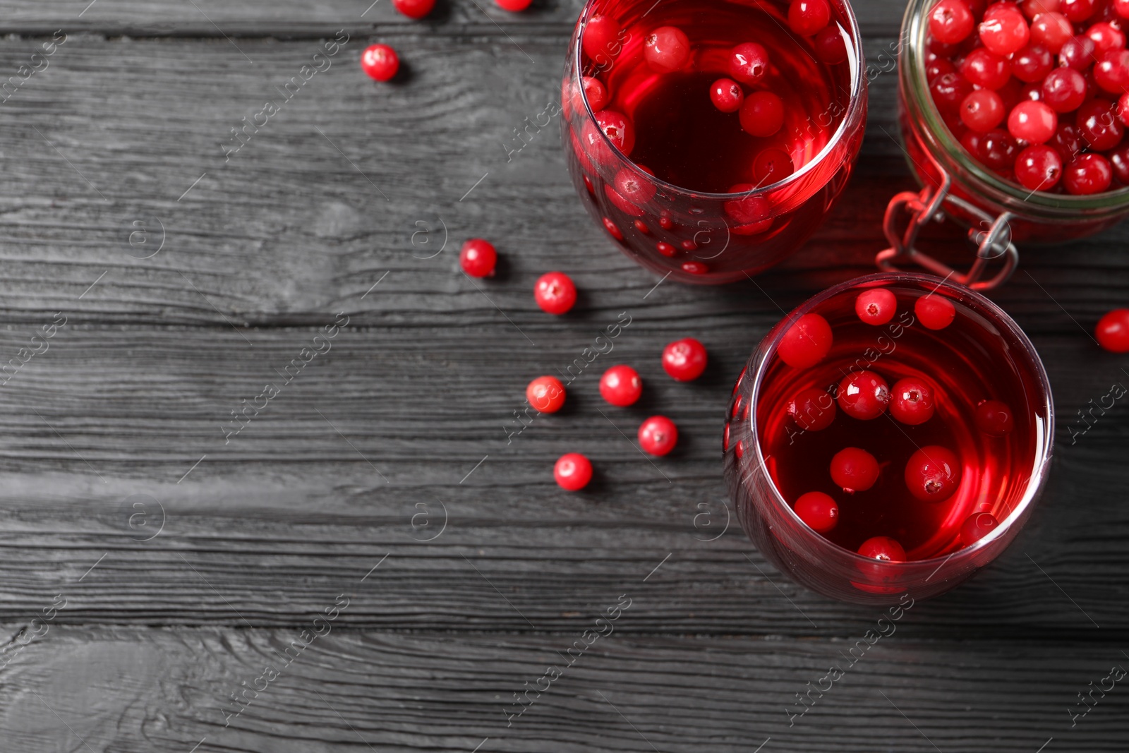 Photo of Tasty cranberry juice in glasses and fresh berries on black wooden table, flat lay. Space for text