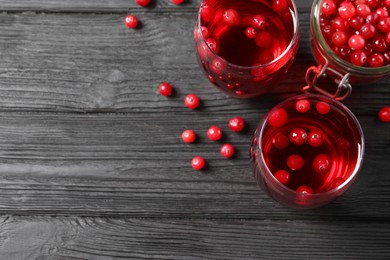 Photo of Tasty cranberry juice in glasses and fresh berries on black wooden table, flat lay. Space for text