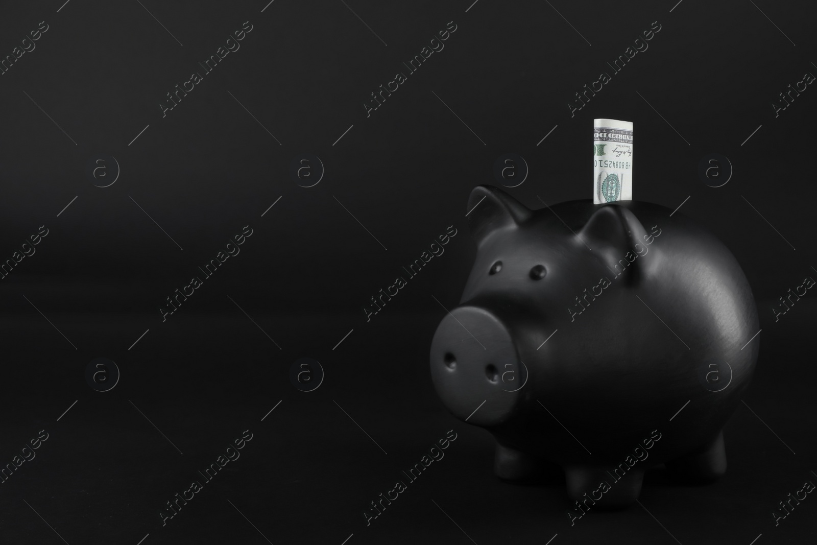 Photo of Black piggy bank with money on table against dark background