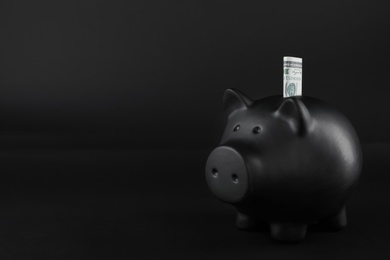 Photo of Black piggy bank with money on table against dark background